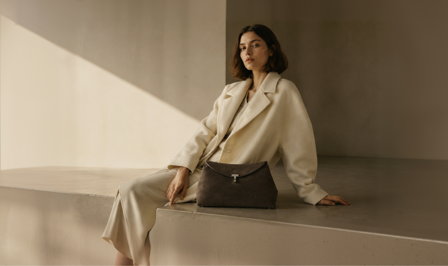 Two figures in oversized cream and camel coats in a concrete gallery.